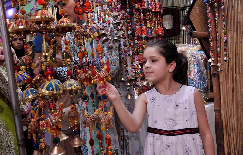 Young girl showing keen interest in traditional stuff on stall during Saqafati Mela promoting Pakistani culture providing entertainment to public at Lok Virsa