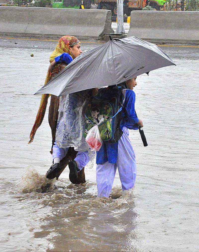 A woman carrying her daughter faces a challenging task of crossing stagnant water amidst heavy rainfall at IJP road