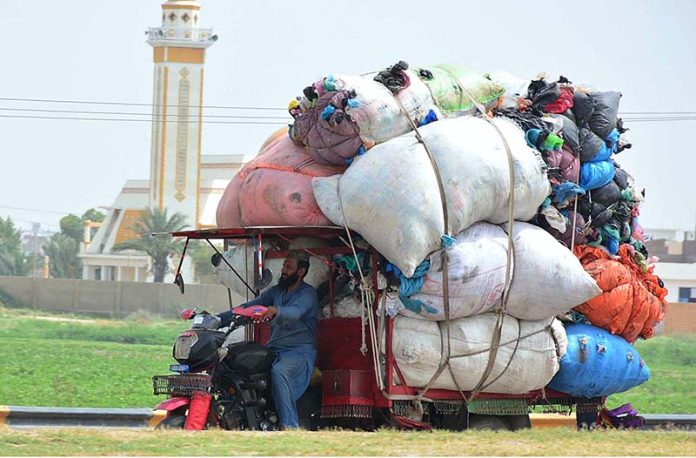 A tri-cycle rickshaw holder on the way loaded with heavy scrap bags at Bypass Road