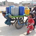 Gypsy children pushing hand cart loaded with water canes after filling from tap at Qasimabad