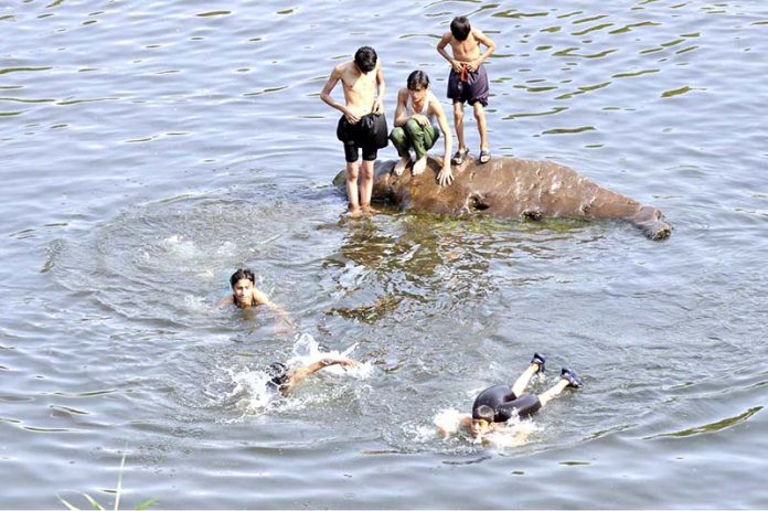 Youngsters swimming to get some relief from hot weather at Rawal Lake spill way stream