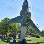Individuals are seeking shelter under the shade of a Fighter Jet Model, providing them respite from the sun at H-8