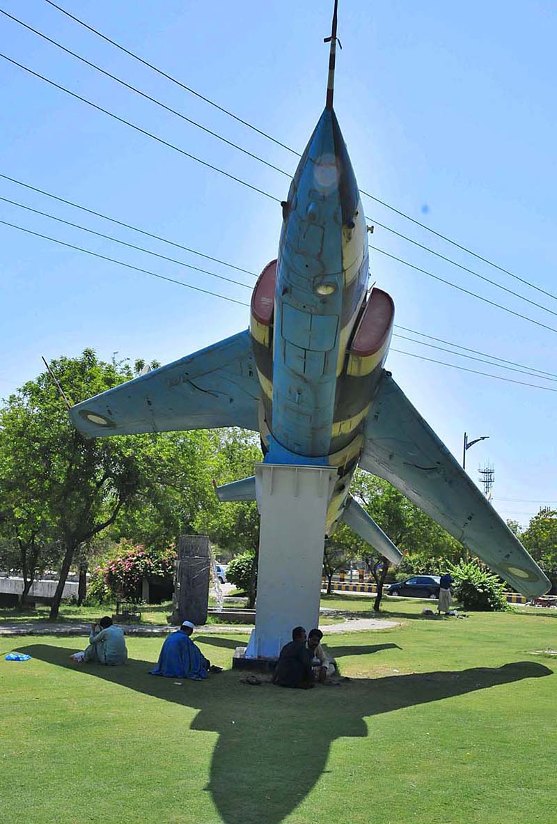 Individuals are seeking shelter under the shade of a Fighter Jet Model, providing them respite from the sun at H-8