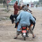 A person carrying sacrificial animal while sitting on rear seat of motorcycle after purchasing from Cattle Market