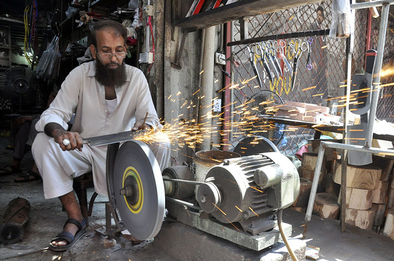 A blacksmith is sharpening knives and axes at his work-place to sell them to the butchers for using them to slaughter sacrificial animals during Eid-ul-Azha