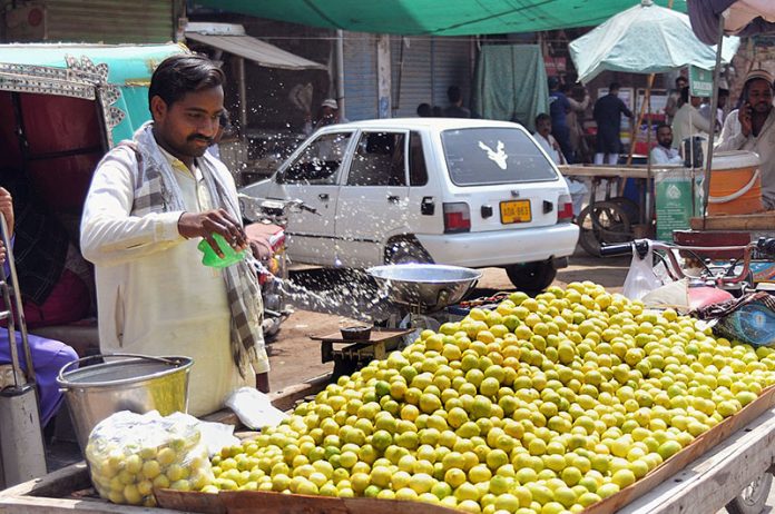 Vendor is busy in sprinkling water on the lemon to keep them fresh at his roadside setup