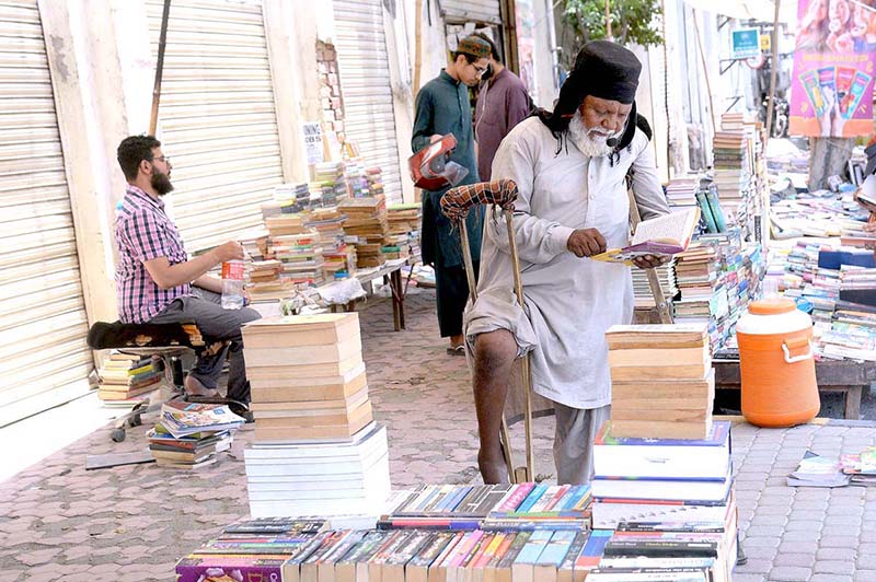 An elderly disabled person selecting books from roadside old books stall in Provincial Capita