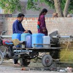 A person with his daughter filling their cans with water from the water pipeline at Fatima Jinnah Town