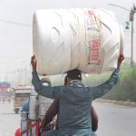 A pillion rider carrying water tank on his head heading towards his destination