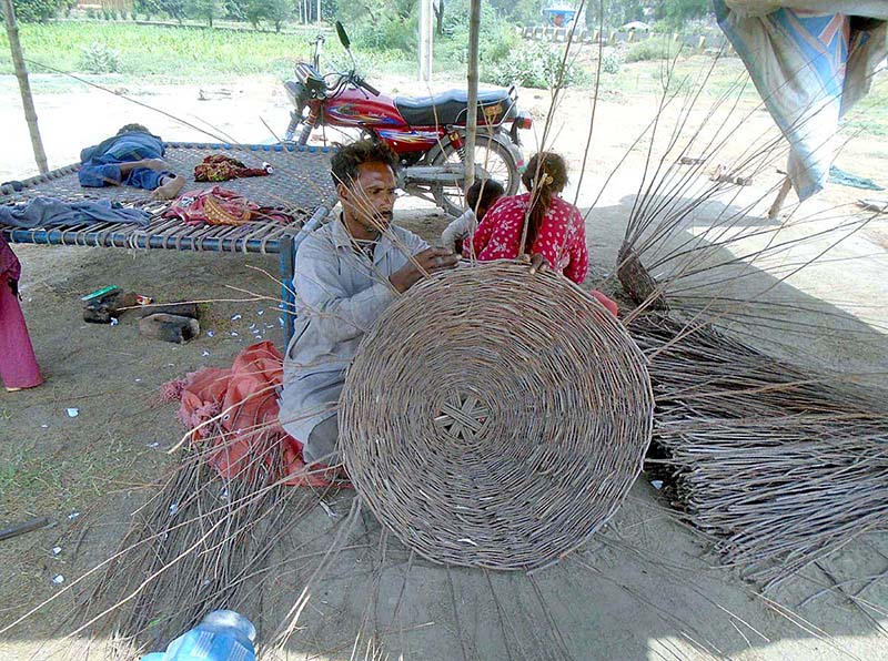 A worker busy in making traditional basket with branches of tree