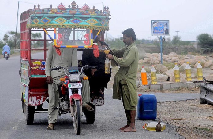 A tri-cycle delivery cart holder purchasing fuel from an illegal petrol selling point along the roadside setup needs the attention of concerned authorities