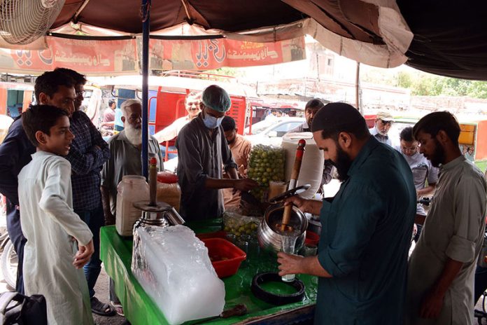 A vendor selling traditional summer drink (Shikanjabeen) to attract the customers at his roadside setup during hot weather.