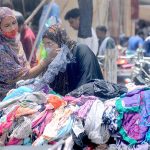 Women selecting and purchasing second-hand clothes displayed by a roadside vendor