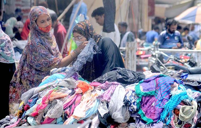 Women selecting and purchasing second-hand clothes displayed by a roadside vendor