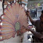 A vendor busy in making handmade wooden decoration items at his roadside setup in the city