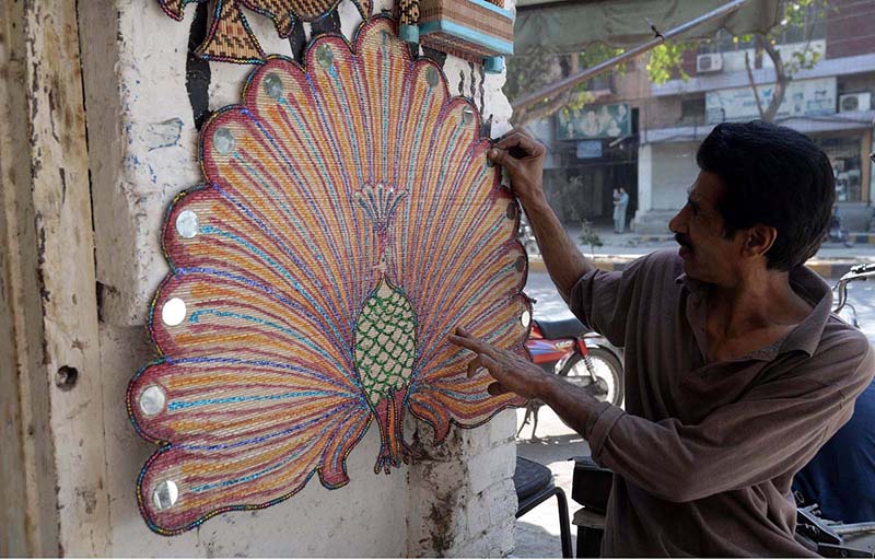 A vendor busy in making handmade wooden decoration items at his roadside setup in the city
