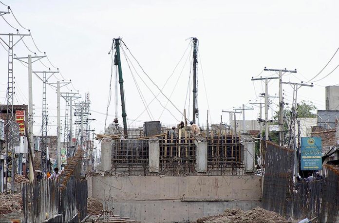 Laborers are engaged in the construction work of a flyover at Muzaffarabad Road