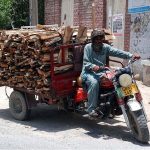 A tri-motorcyclist on the way loaded with woods