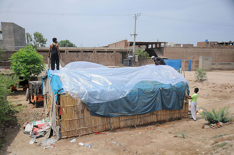 Gypsy people covering their makeshift home with polythene sheets to protect them from the rain near Vehari Chowk