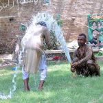 A man bathing at a water tap to get some relief from hot weather