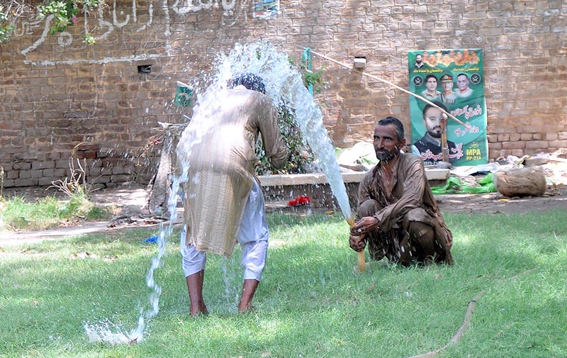 A man bathing at a water tap to get some relief from hot weather