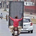 A person holding iron door while sitting on rear seat of motorcycle