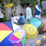 An aged man is displaying and selling umbrella at roadside in the city