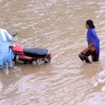 Motorcyclist passing through rain water accumulated on the road during rain in the city