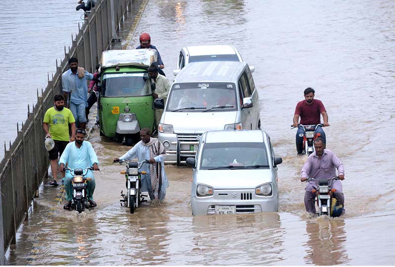 Motorcyclist passing through rain water accumulated on the road during rain in the city