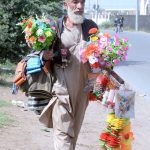 An elderly vendor displaying decorative stuff for sale to attract customers while shuttling on the road