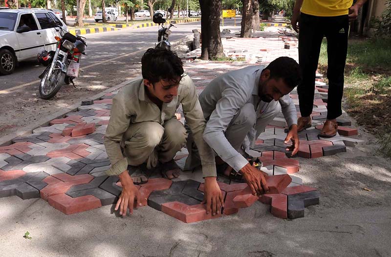 Labourers busy in fixing tuff tiles on footpath in Federal Capital