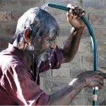 A man bathing from water tap to get some relief from hot weather
