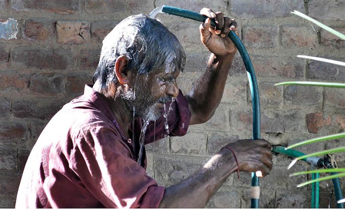 A man bathing from water tap to get some relief from hot weather