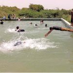 Youngsters jumping into a swimming pool for bathing to get some relief from hot weather in the city