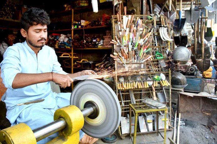 A vendor sharpening the knife to be used for slaughtering the sacrificial animals during Eid ul Azha