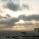 As the sun begins its descent, a breathtaking scene unfolds with its radiant glow peeking through a mesmerizing tapestry of dark clouds, painting the sky with a captivating blend of light and shadow