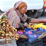 An elderly woman arranging fruits to attract the customers at his roadside setup