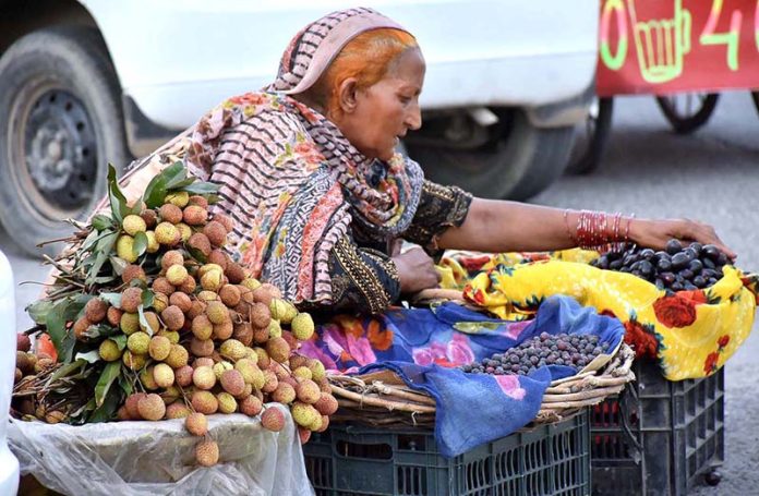 An elderly woman arranging fruits to attract the customers at his roadside setup