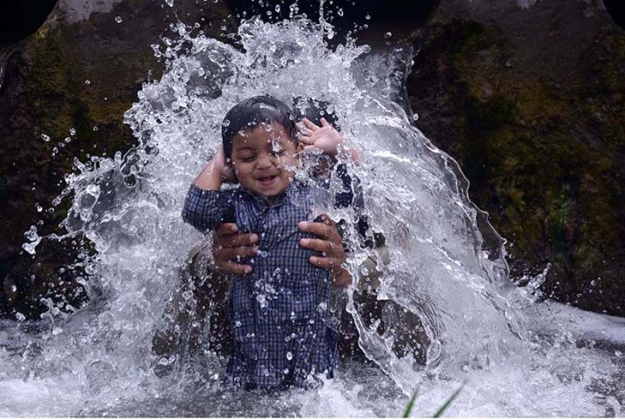 A child enjoying a bath in a stream with his father to get some relief from hot weather at Dando Pull Musazai area