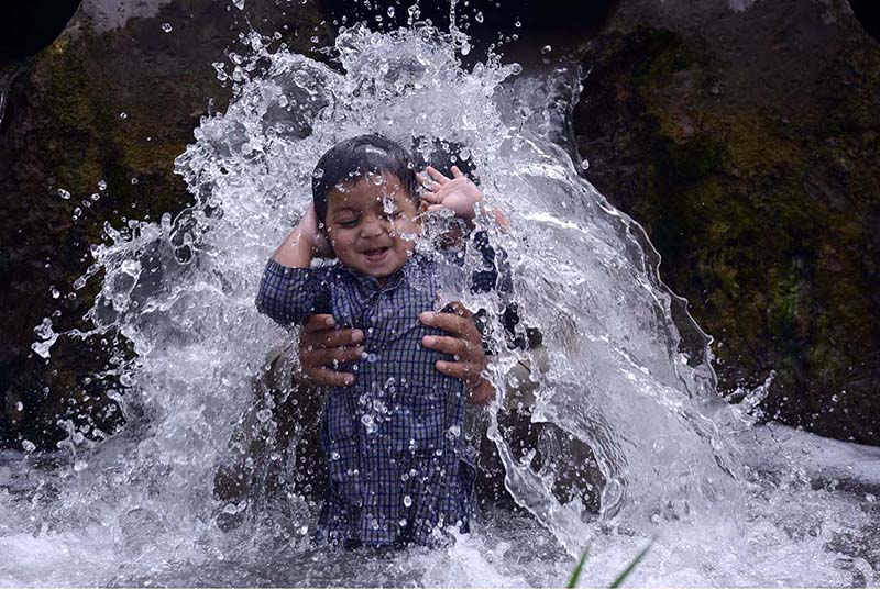 A child enjoying a bath in a stream with his father to get some relief from hot weather at Dando Pull Musazai area