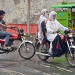 Young girl riding a motorbike along with her mother heading towards their destination during rain in Provincial Capital City