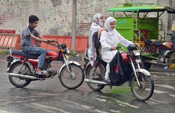 Young girl riding a motorbike along with her mother heading towards their destination during rain in Provincial Capital City