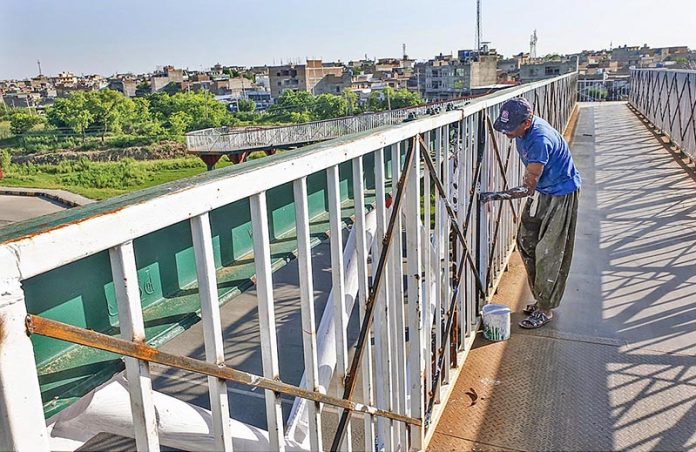 A painter busy in painting a pedestrian bridge on Islamabad Expressway