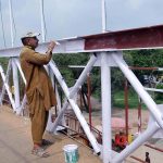 The painter paints the metal railings of the pedestrian bridge with white paint at Islamabad Expressway.
