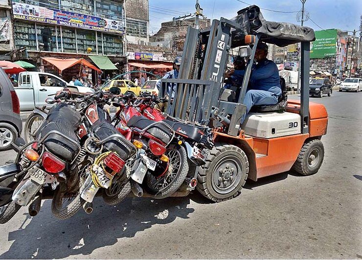 A traffic police official removing the wrongly parked motorbikes with fork lifter from "No Parking Area" at Raja Bazaar