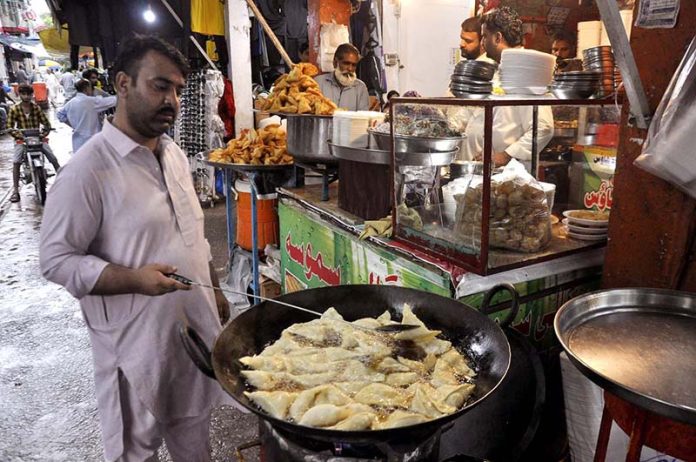 A vendor busy in frying traditional food item (samosa) for customers during rain at his shop in the Federal Capital.