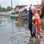 People passing through rain water accumulated at Railway Colony area after heavy rain in the city