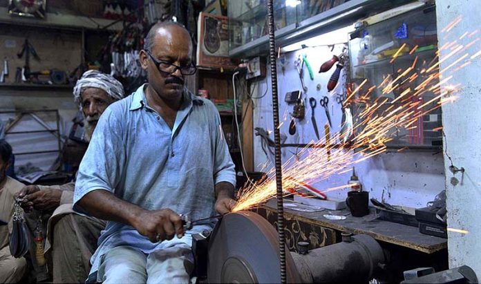A blacksmith busy in sharpening the knives to be used by mourners oozing themselves during procession of Muharram ul Haram