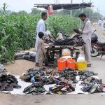 A vendor selling shoes to customers at his roadside setup