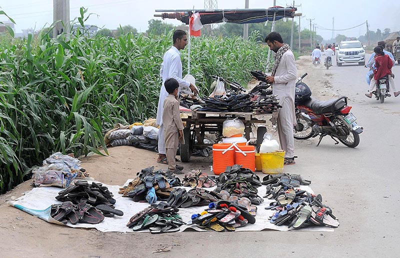 A vendor selling shoes to customers at his roadside setup